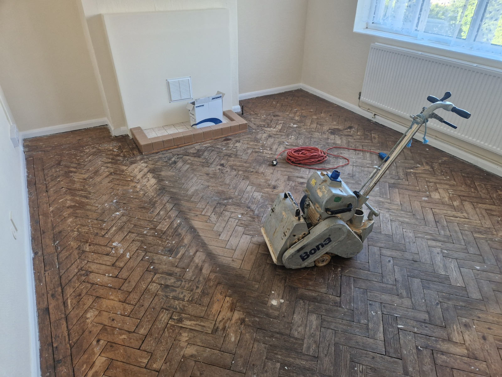 Parquet Floor Sanding in Bicester on an oak herringbone parquet floor, mid-sanding with a professional Bona belt sander in a living room